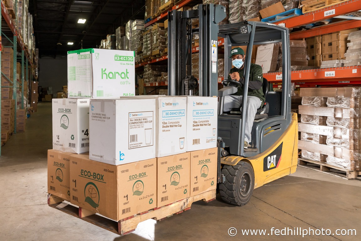 A corporate business photo of an employee in a warehouse operating a forklift loaded with boxes of product.