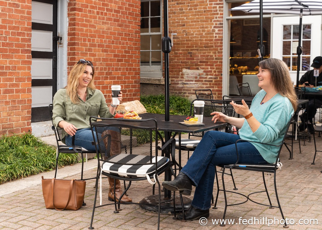 Tourism/lifestyle/restaurant photo of two people laughing at a cafe table set with food and beverages.