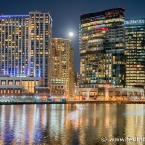 Fine art photo of moonrise over Harbor East hotel and office buildings reflected in water in Baltimore City, Maryland.