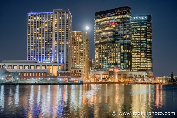 Fine art photo of moonrise over Harbor East hotel and office buildings reflected in water in Baltimore City, Maryland.