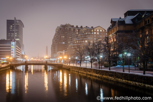 Fine art photo at night with snow, jones falls, Scarlett Place, Public Works Building, and bridge in downtown Baltimore MD.
