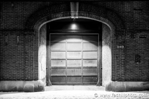 Fine art black and white photograph of footprints in snow past a fire station at night in Baltimore City, Maryland.