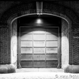 Fine art black and white photograph of footprints in snow past a fire station at night in Baltimore City, Maryland.