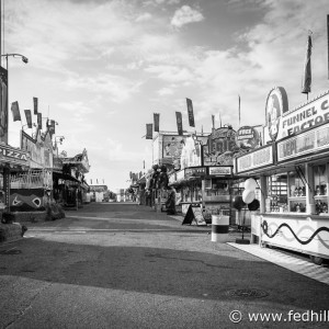 Fine art black and white photograph of the empty midway on a morning at the Maryland State Fair. Vendors selling french fries, funnel cake, and games.