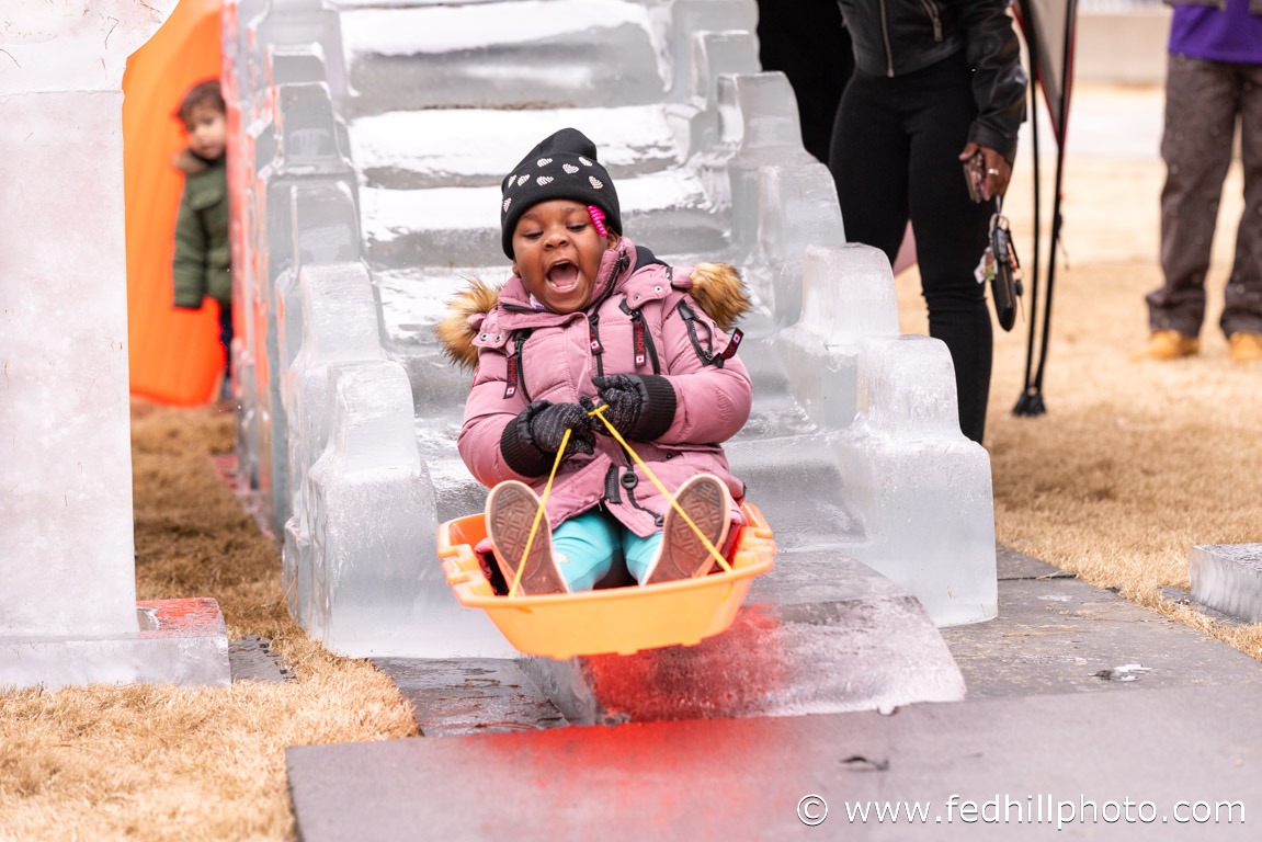 Holiday community event photo of a child riding a sled down an ice slide.