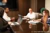 Corporate business photo of four people in a corporate setting at a conference room table conversing.